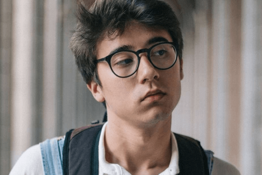 A highschool student with glasses and backpack looking away