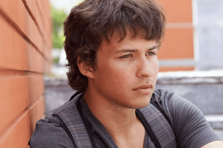 A teen boy looking away while leaning towards an orange wall