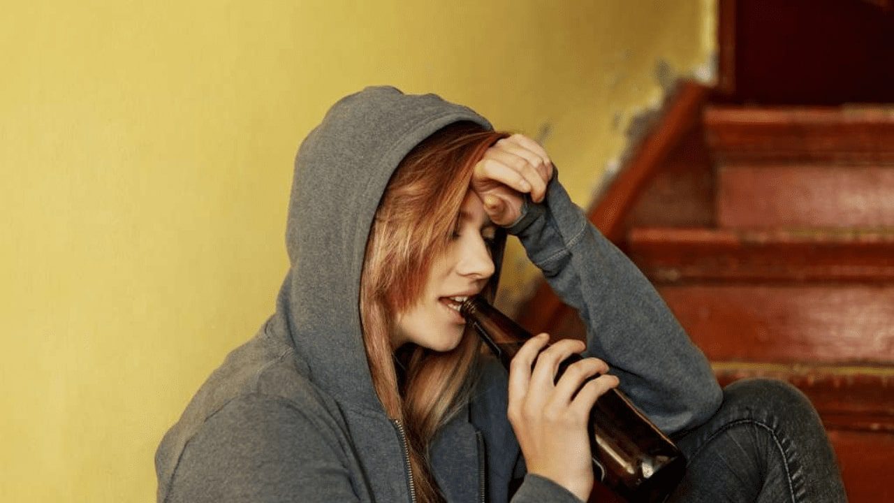arafed woman in a hoodie drinking a beer while sitting on the stairs