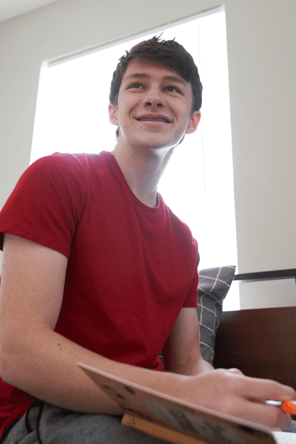 arafed man sitting on a bed with a laptop and a pen