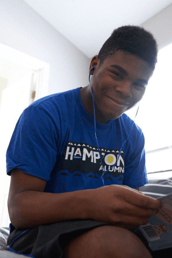 boy sitting on bed with headphones on and reading a book