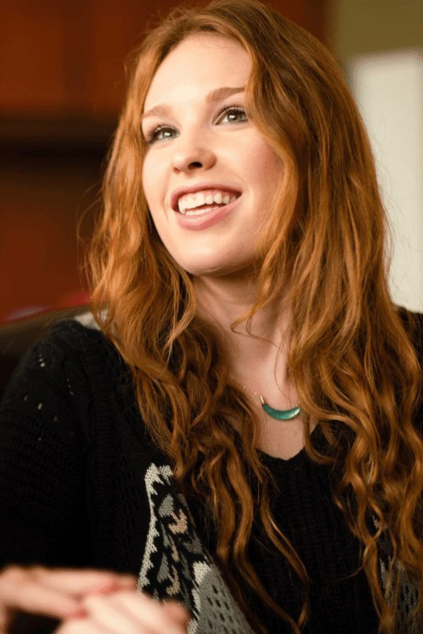 arafed woman with long red hair sitting in a chair and smiling