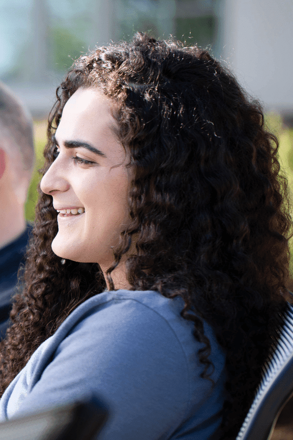 smiling woman with curly hair sitting in a chair with a man in the background
