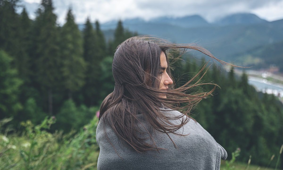 A young woman wrapped in a plaid in the mountains on a blurred background, copy space.