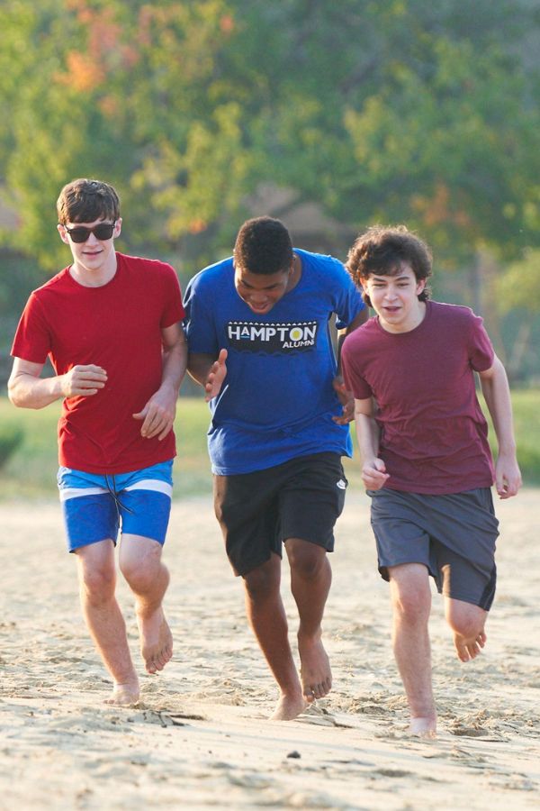 three young men running on a beach with a frisbee in hand