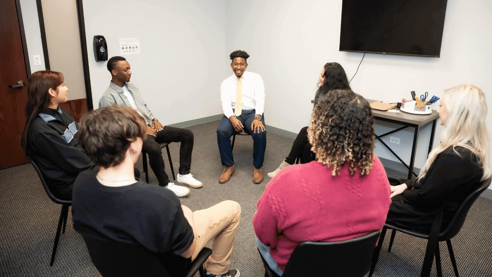 several people sitting in a circle in a room with a tv