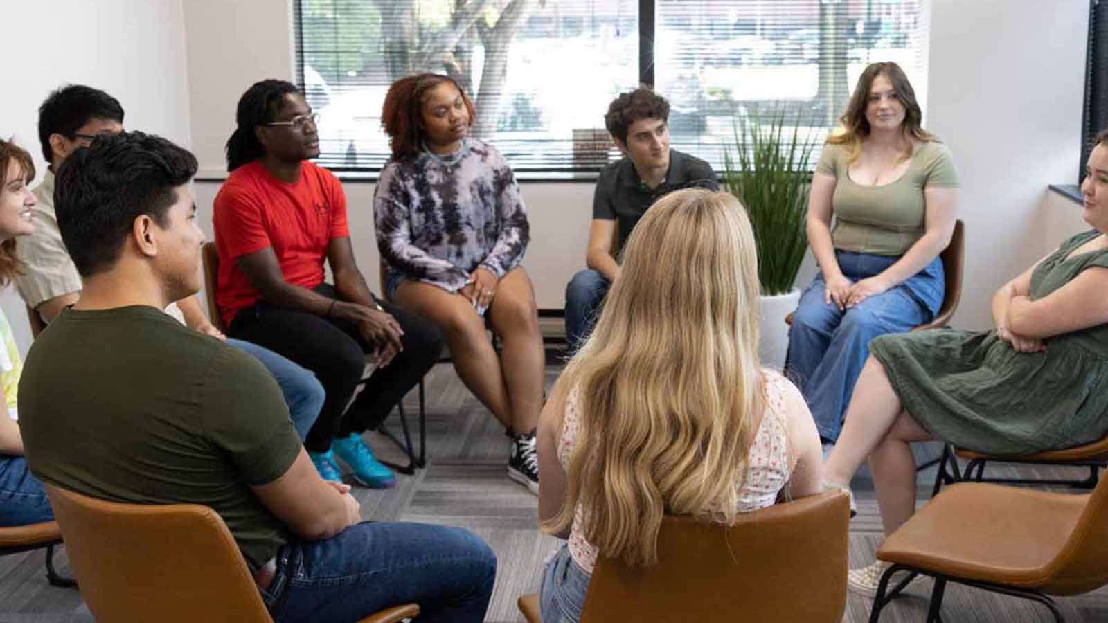 several people sitting in chairs in a circle talking to each other