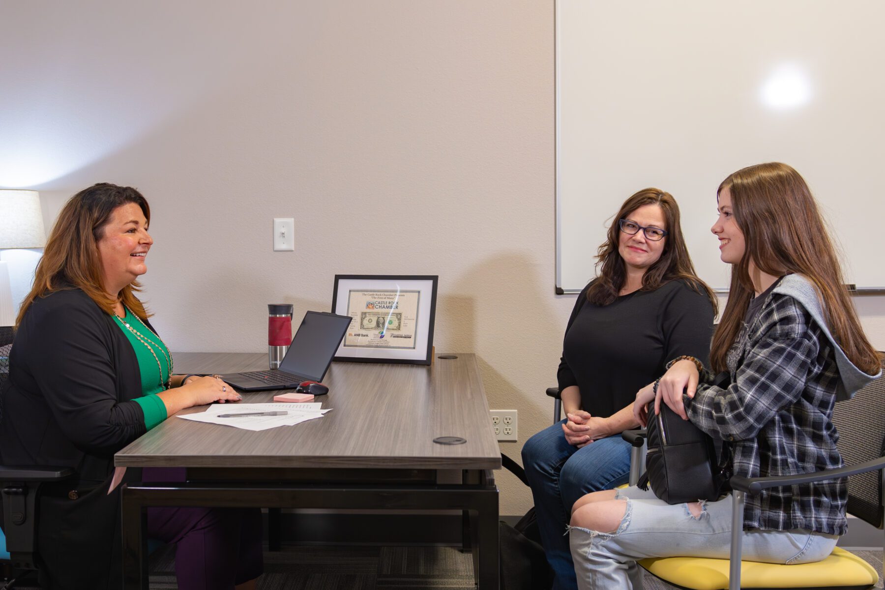 A parent and teen sit across from a therapist, smiling.