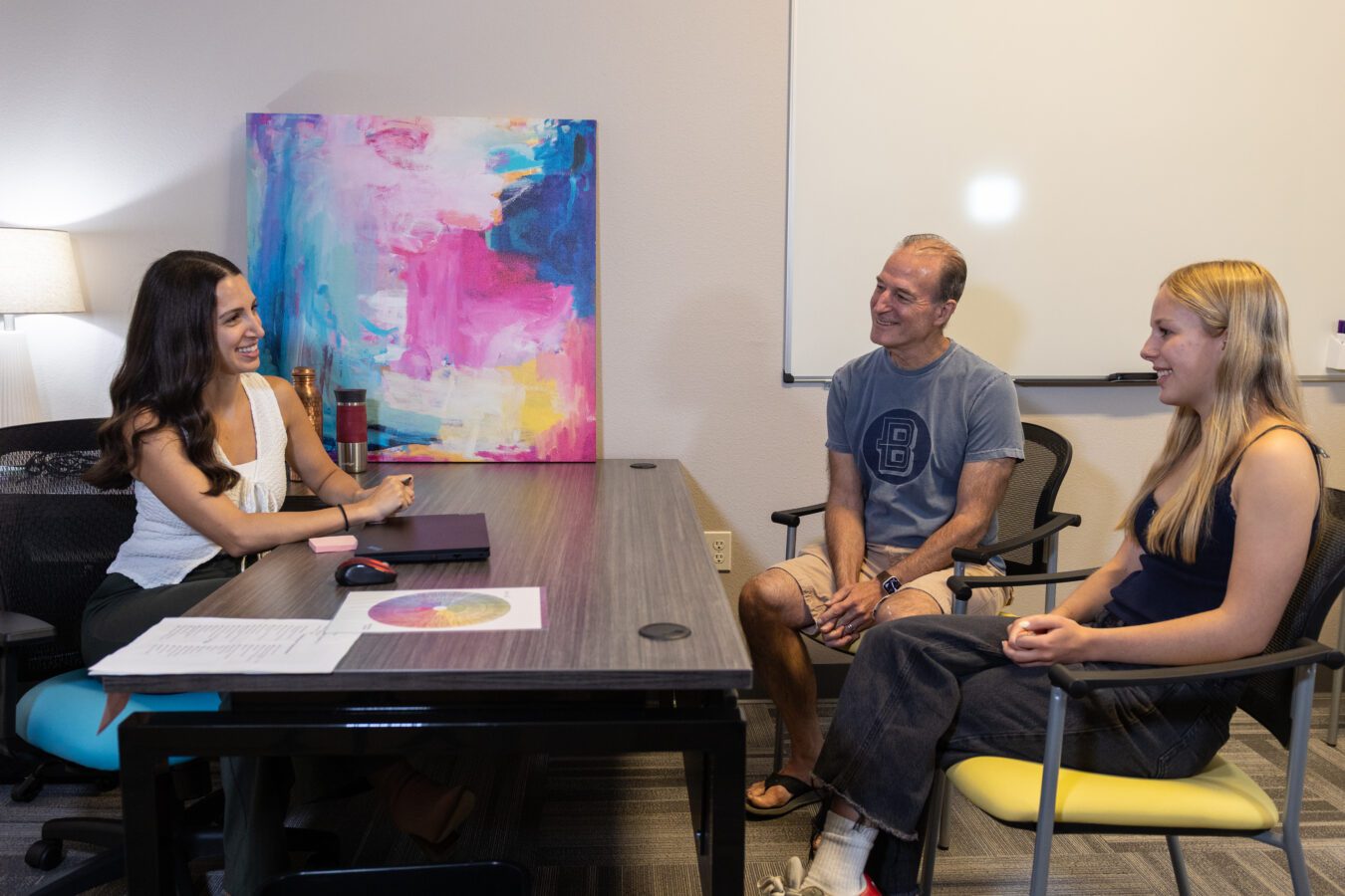 A father and daughter sit across from an admissions coordinator, smiling